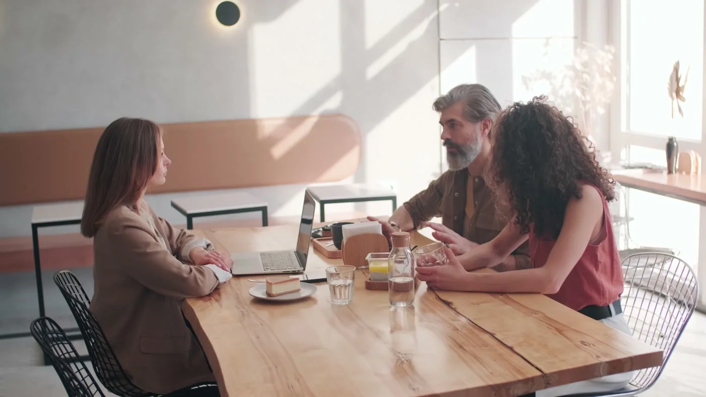 Two agents in a breakfast meeting at a café table, laptop open.