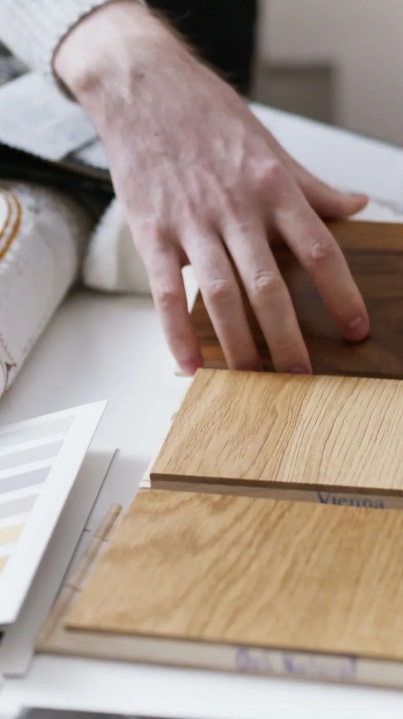 A designer’s hands sort wood and fabric samples.