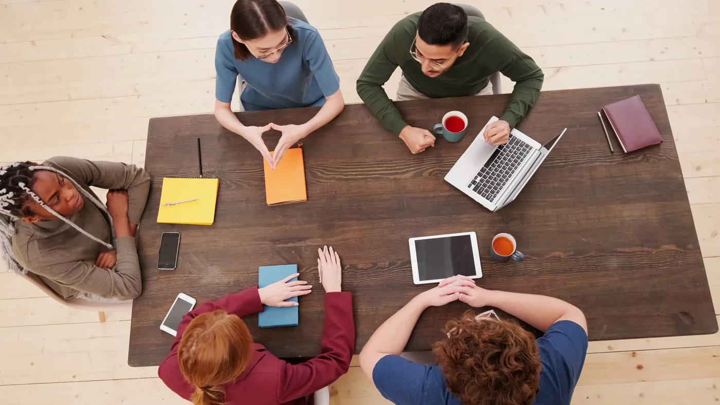 Overhead view of a working table: laptops, tablets, notebooks and coffee.