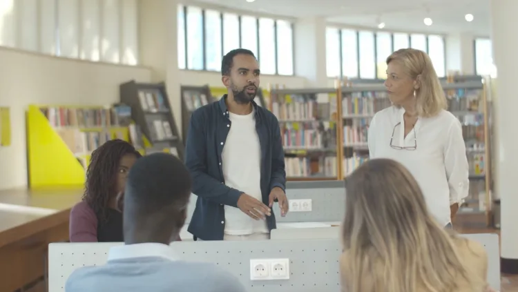 A guest speaks to a small seated group between library shelves.