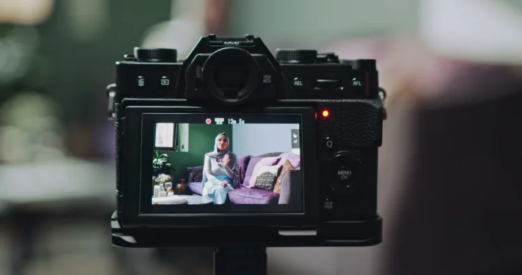 A camera on a tripod, a woman in a living room on its screen.