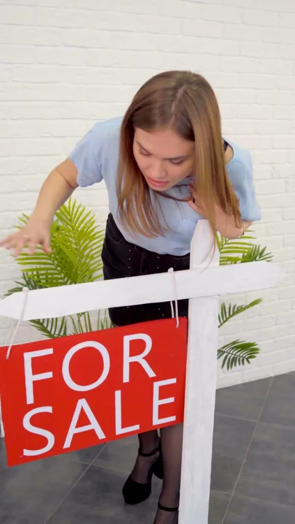 A woman straightens a For Sale sign in a yard.