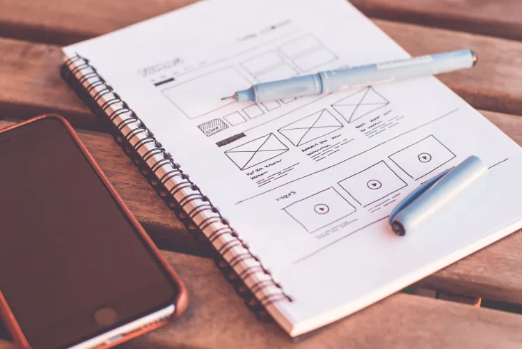 A hand-drawn website wireframe in a notebook on a desk.